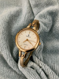 A gold-tone women's watch with a round cream dial and bangle bracelet