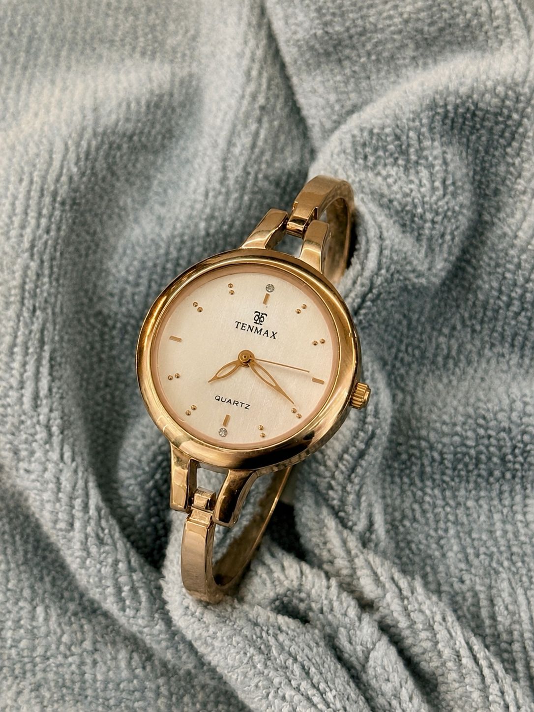 A gold-tone women's watch with a round cream dial and bangle bracelet
